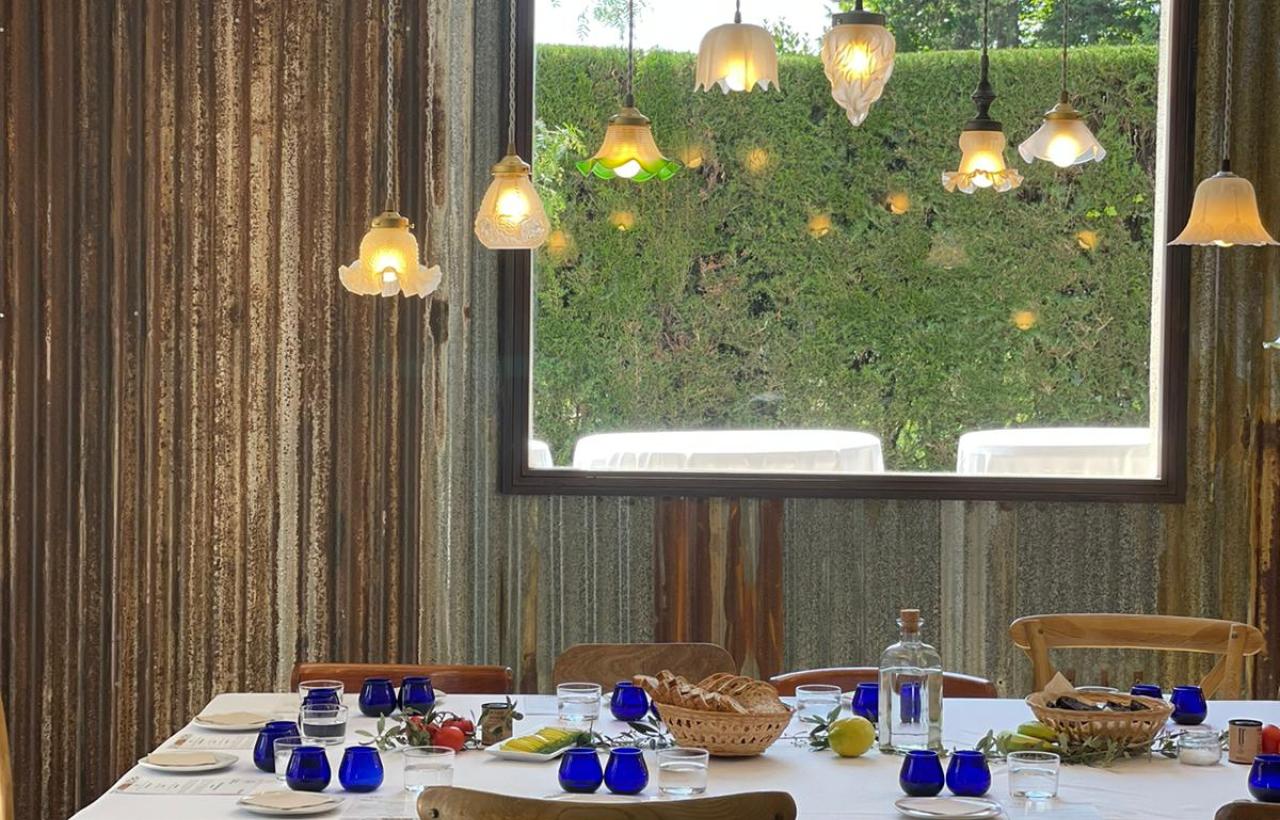 Photo of the tasting room in which you can see the table set, with the glasses for the official Oil Tasting, the lampshades that illuminate the table and the window overlooking the gardens